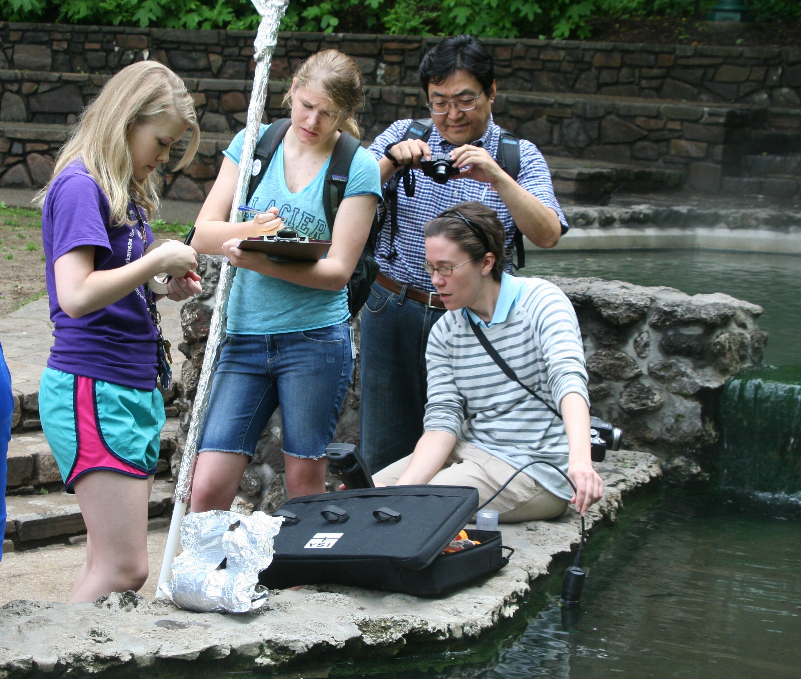 Four people gather around water testing equipment next to a thermal spring. 