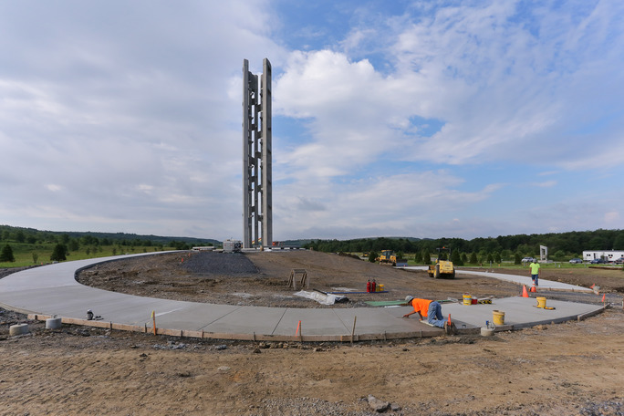A construction worker smooths out the concrete sidewalk leading up to the Tower of Voices. The tower is in the distance.