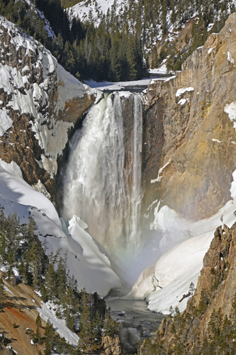 Tall waterfall with snow at the bottom and rainbow in the spray at the bottom