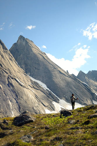 Ranger stands next to a tall gray jagged mountain.