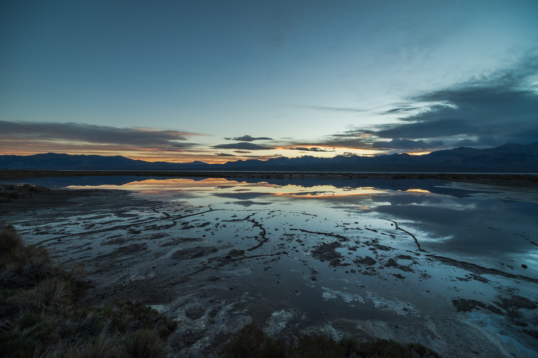 A large pool of water with mountains reflected in the background and a darkening sky.