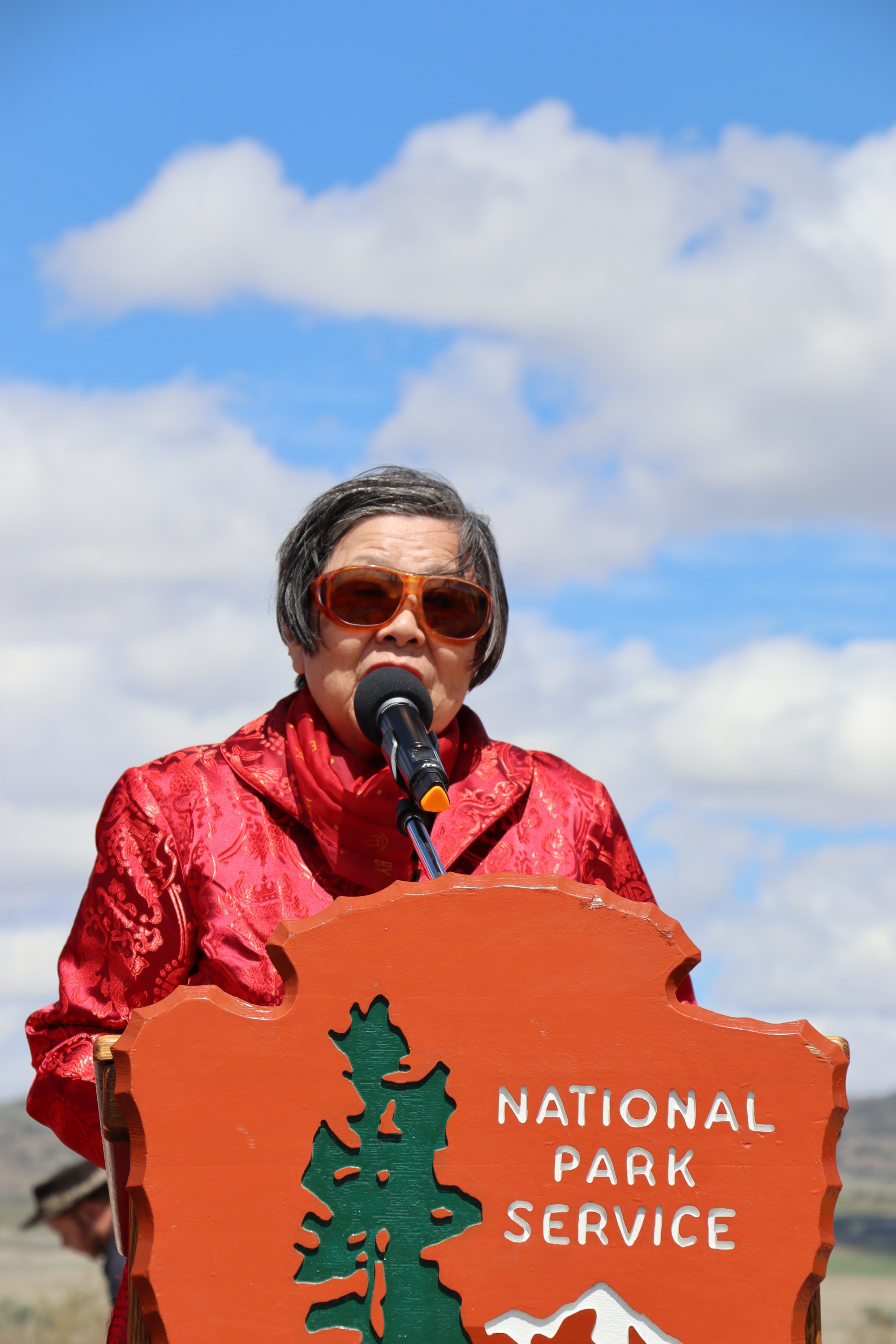 Chinese speaker standing in front of podium with blue skies and mountains in the background.
