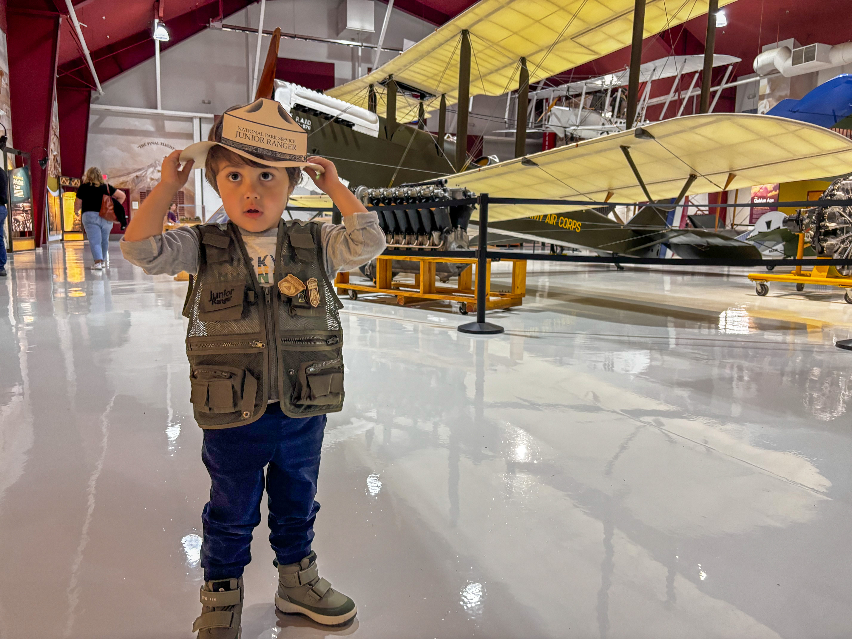 A child with a junior ranger cutout head band, behind him is a plane display. 