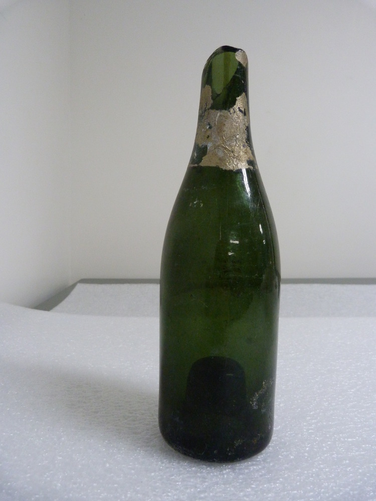 color photo of green glass bottle with top broken off and gold paper remnants around the neck
