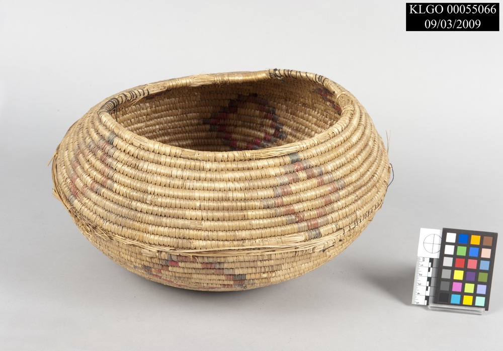 color photo of a beach grass basket that is circular in shape with faded red and blue diamond shapes throughout
