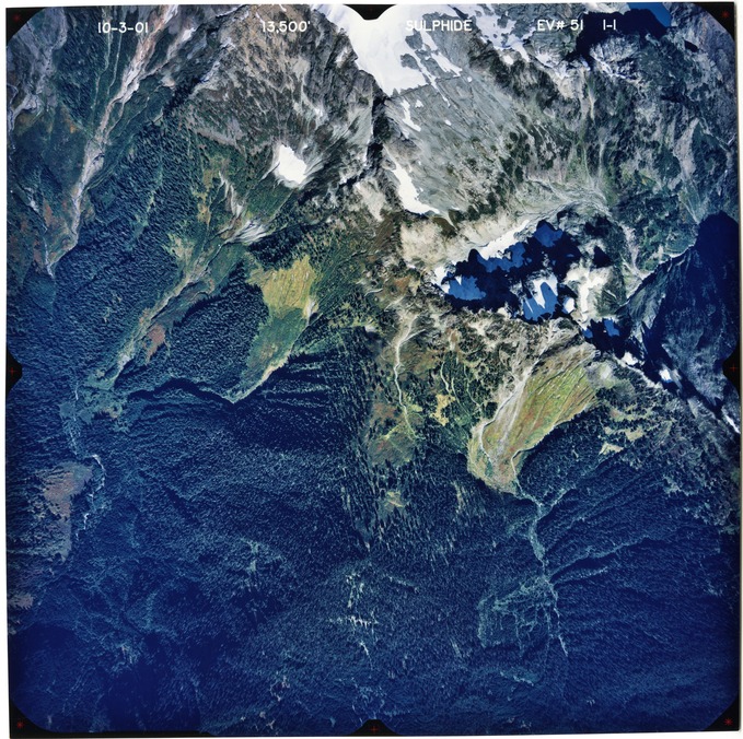 Color aerial photograph of glaciated mountain peak with forested valleys below.