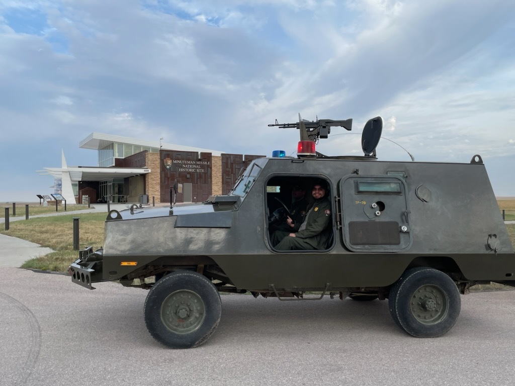Park Ranger in green park service uniform sitting in a green armored vehicle with a machine gun on top. 