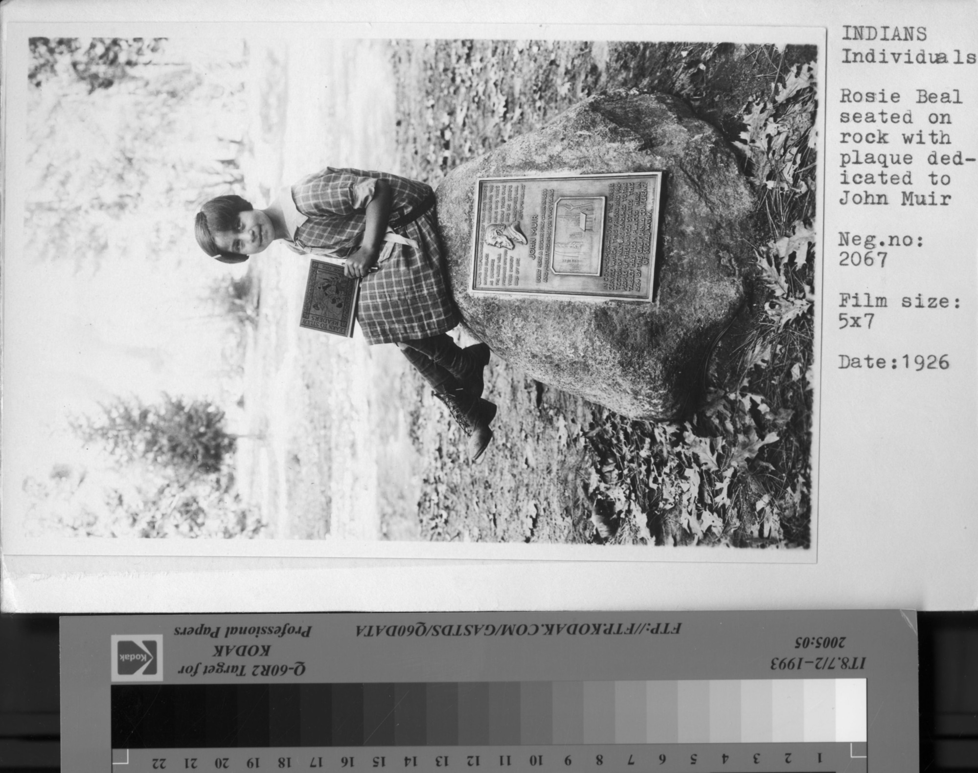 Rose Beal seated on rock with plaque dedicated to John Muir.