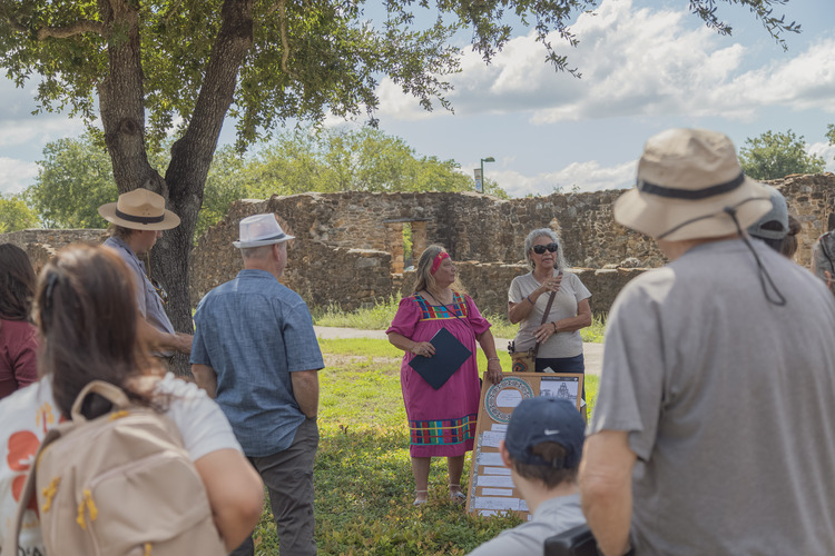 Two women talking to a larger group under a tree