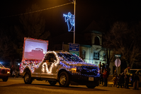 Truck with strings of lights, slide show on screen in the back under a light angel at night in town.