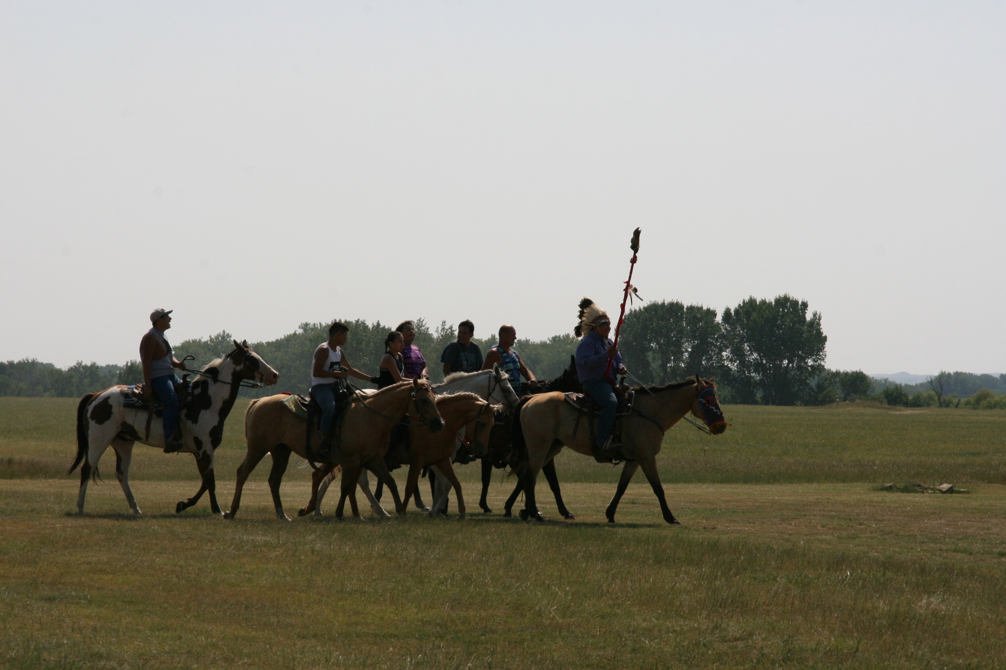 Several American Indian men riding horses through a grassy field