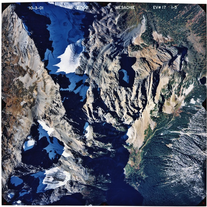 Color aerial photograph of glaciated mountain peak with forested valleys below.
