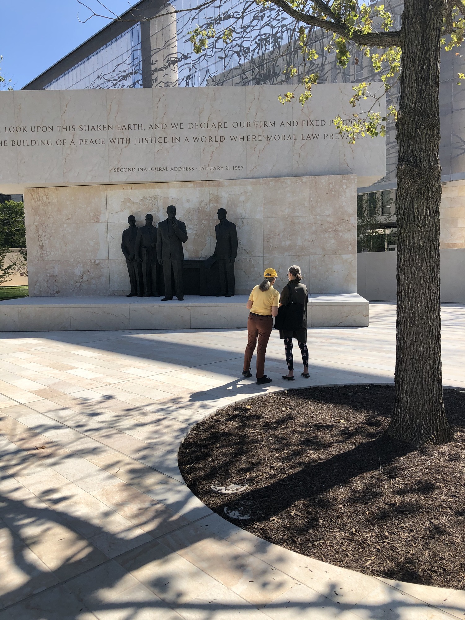 A volunteer in a yellow uniform stands with a visitor in front of the presidential grouping of statues at the Dwight D. Eisenhower Memorial 