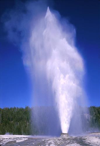 Beehive Geyser with rainbow, visitors, and Old Faithful Lodge in background