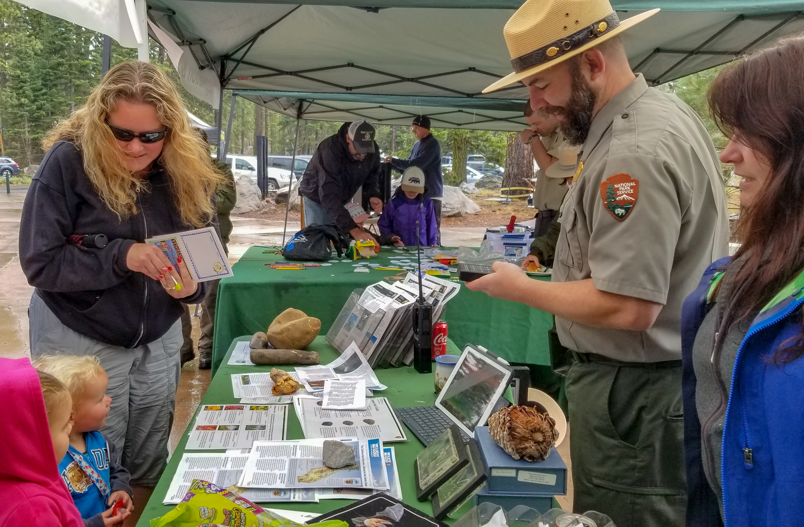 Two young girls and a woman stand on side of a table. A park ranger holds a device that plays animal sounds. 