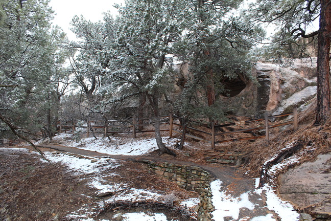 White snow lightly covers the ground as a trail turn to the left and behind it a crevise in the rock face.