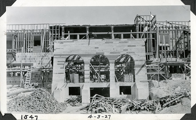 This is an historic black and white photograph from the Scotty's Castle Historic Photograph Collection, Death Valley National Park of Scotty's Castle Main House, looking north. Earth excavated in front of Lower Music Room wall. Stacked hollow tile and brick work in same area. Large pile of bricks being used around window framing. April 3, 1927. Photographed by Mat Roy Thompson.