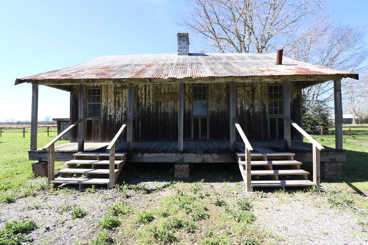 Wooden structure with metal roofing, centralized chimney, and front porch.