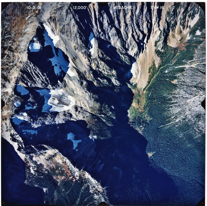 Color aerial photograph of glaciated mountain peak with forested valleys below.
