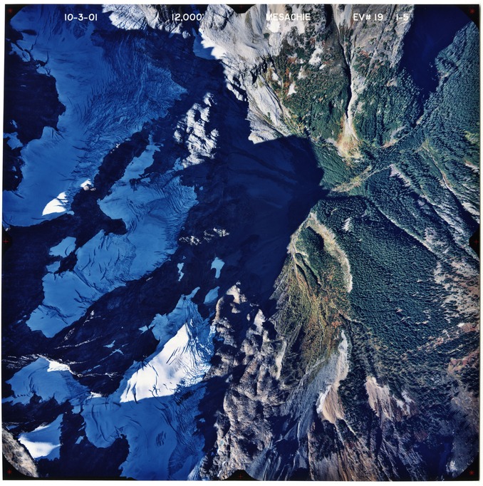 Color aerial photograph of glaciated mountain peak with forested valleys below.