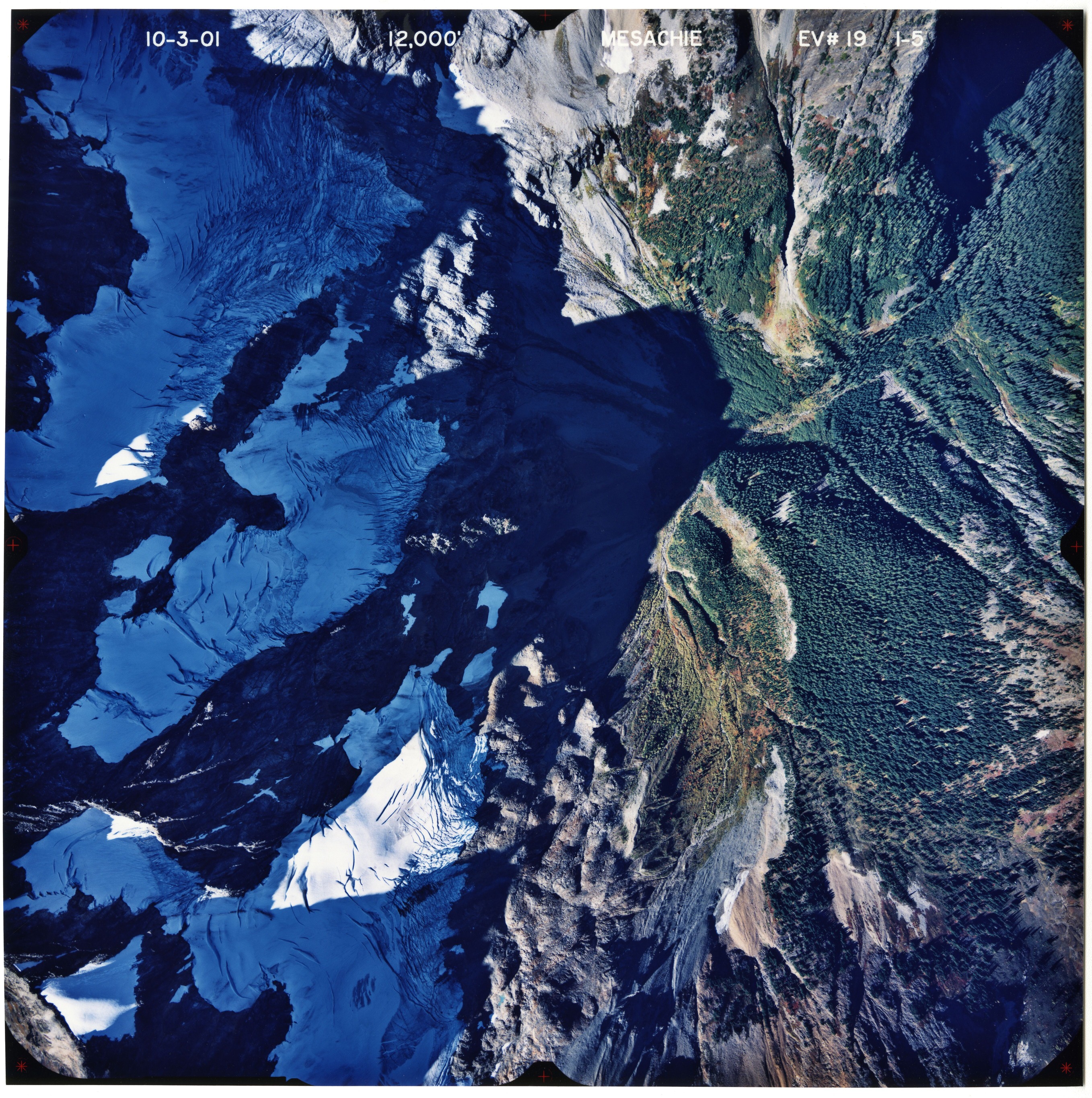 Color aerial photograph of glaciated mountain peak with forested valleys below.