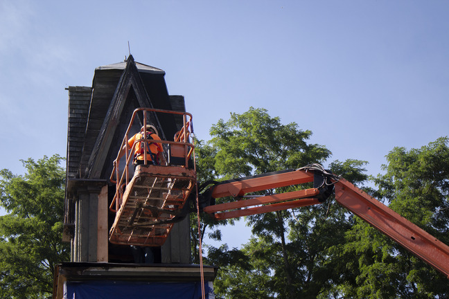 A construction worker wearing a harness prepares to enter the steeple from a lift.