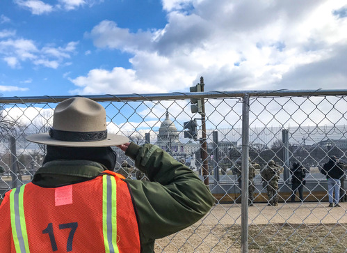 Park ranger saluting towards the U.S. Capitol building through a fence