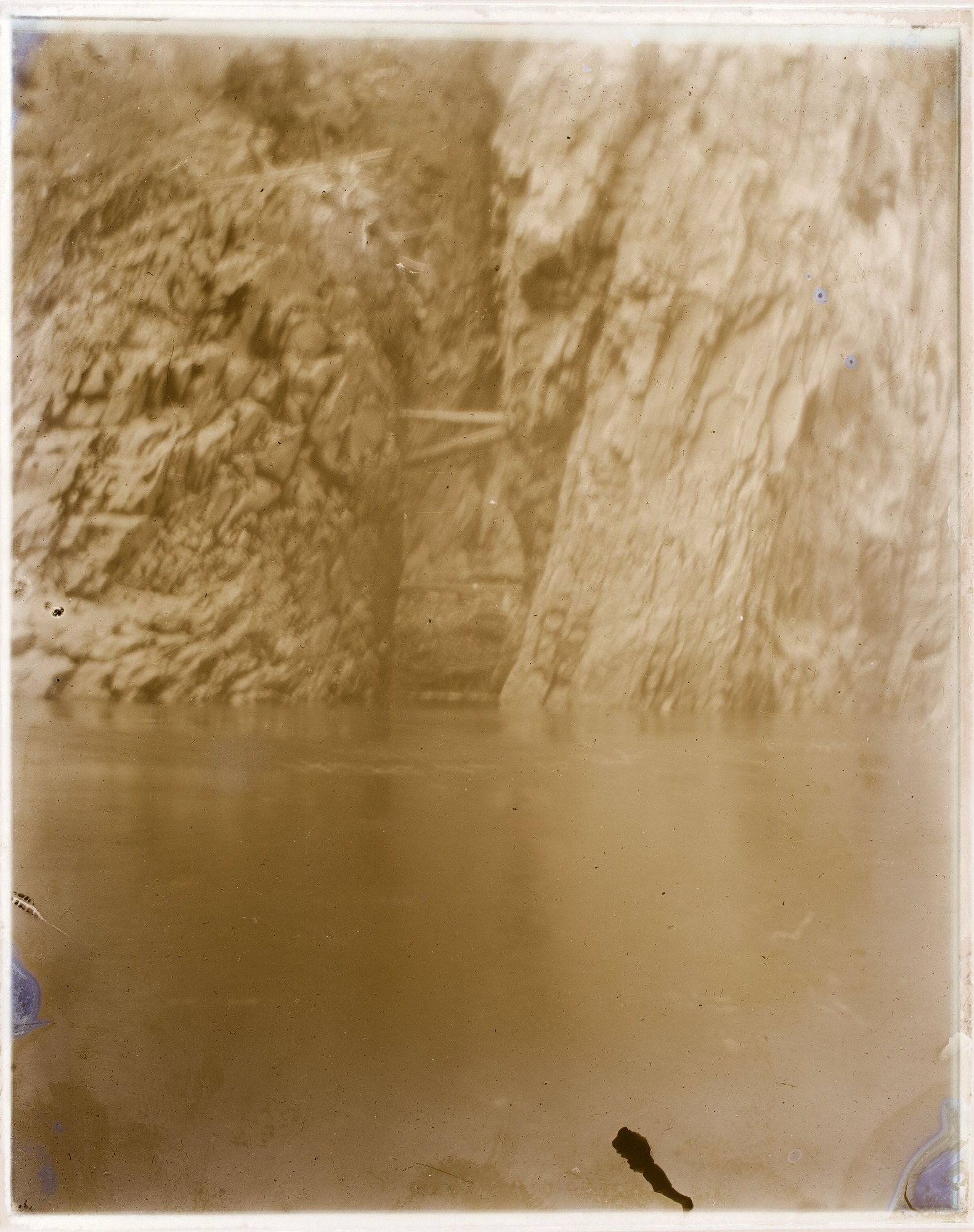 A calm river is in the foreground with steep canyon walls in the background.