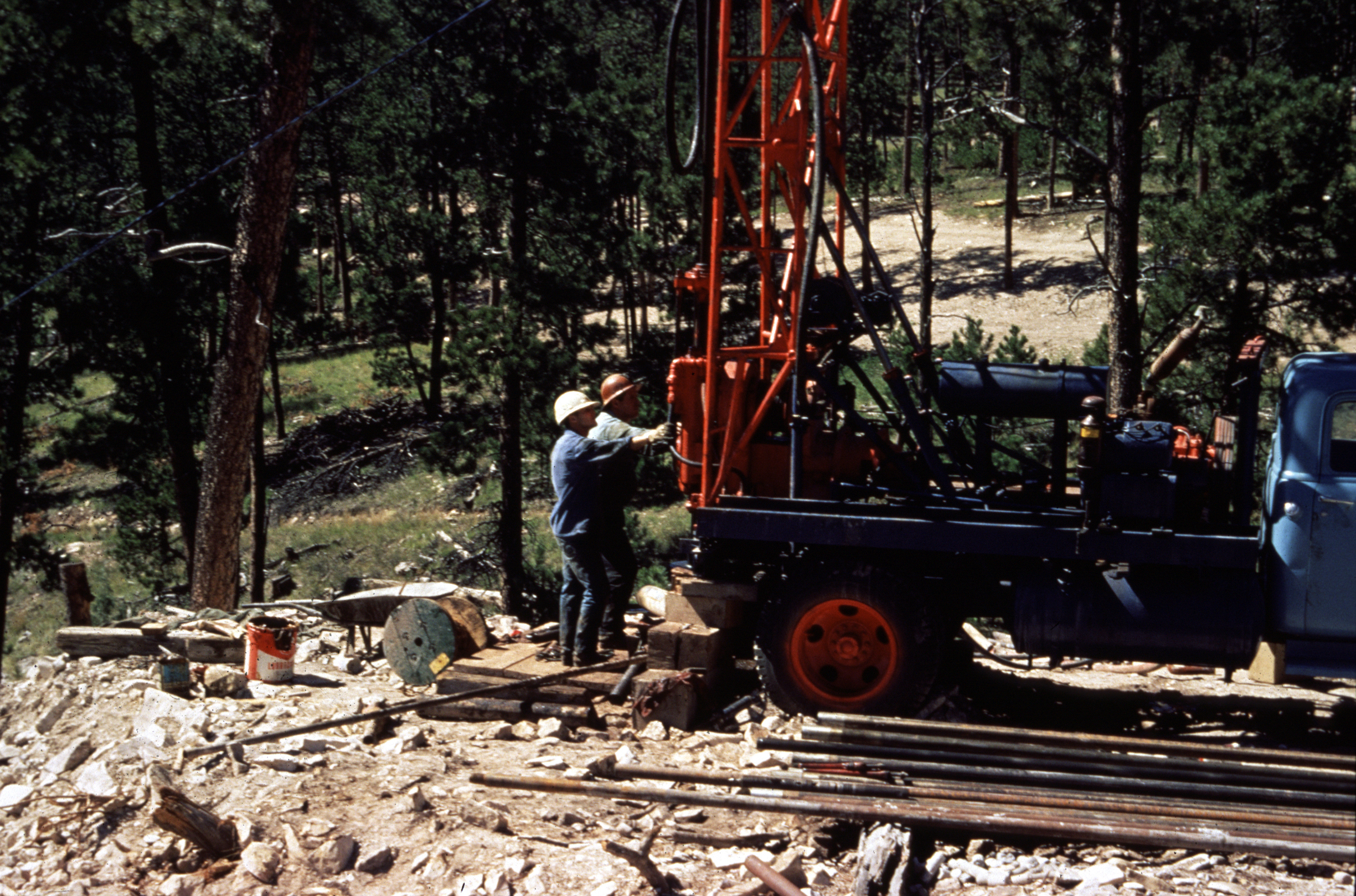 Two men with truck mounted drilling rig and trees in background 