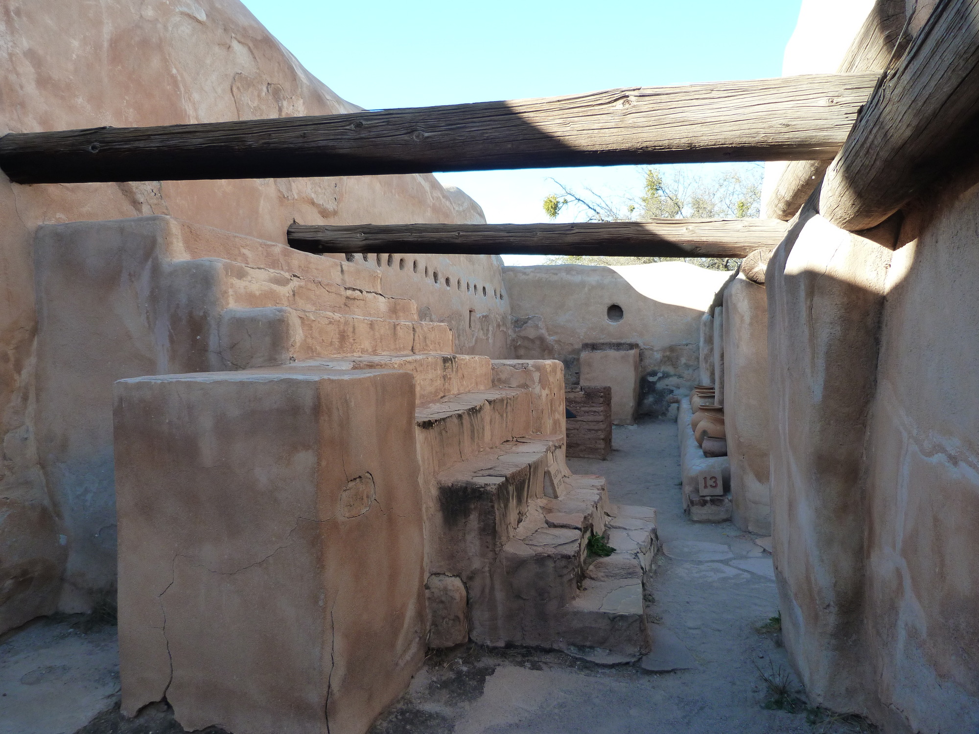 Storeroom with large steps in foreground, viga (beams) overhead and pots along bench in background