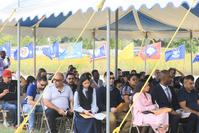 Rows of chairs under a large tent are filled. There is a row of state flags visible behind the tent.