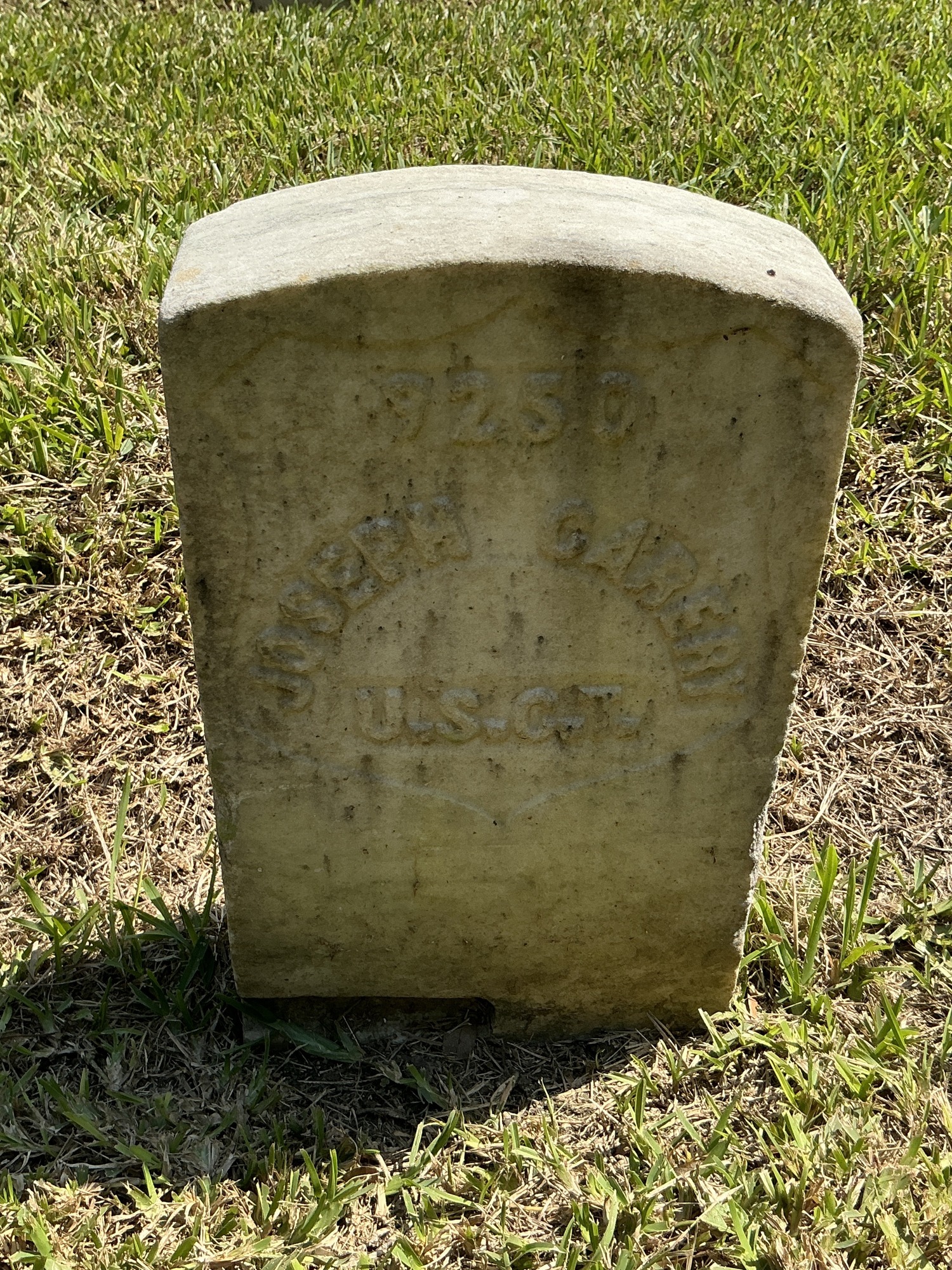 Front of historic upright marble headstone with recessed shield with recessed lettering face.
