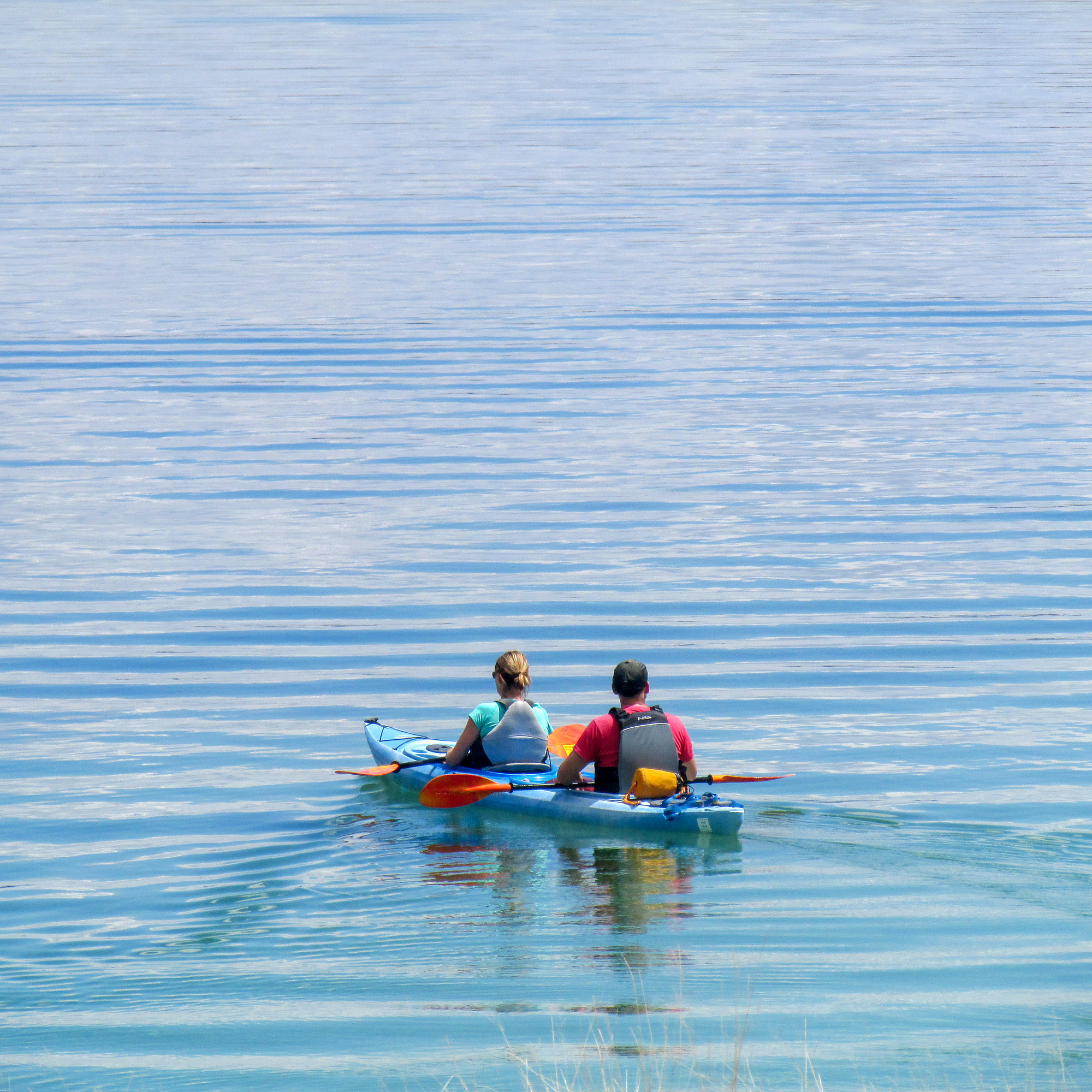 A couple sits in a tandem kayak resting their paddles on a lake.