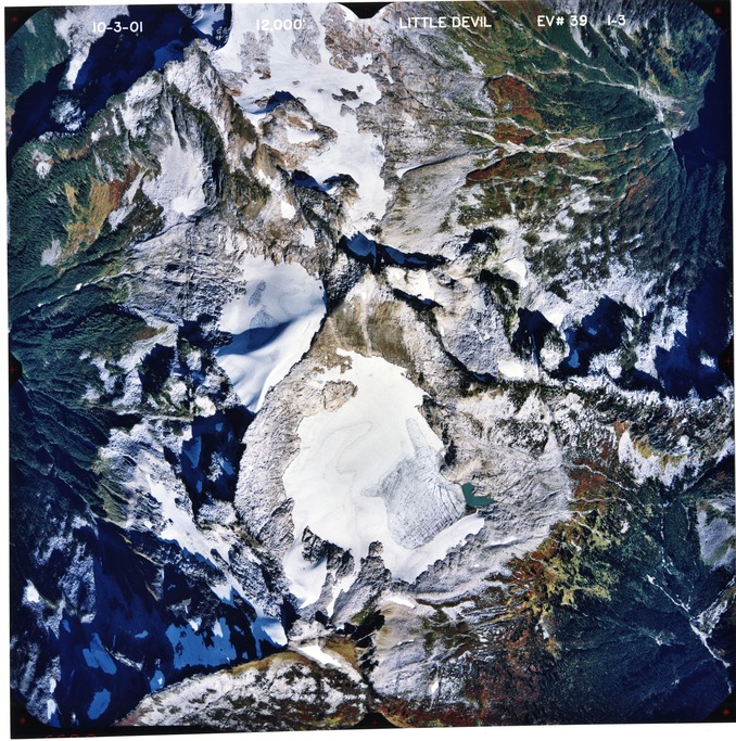 Color aerial photograph of glaciated mountain peak with forested valleys below.
