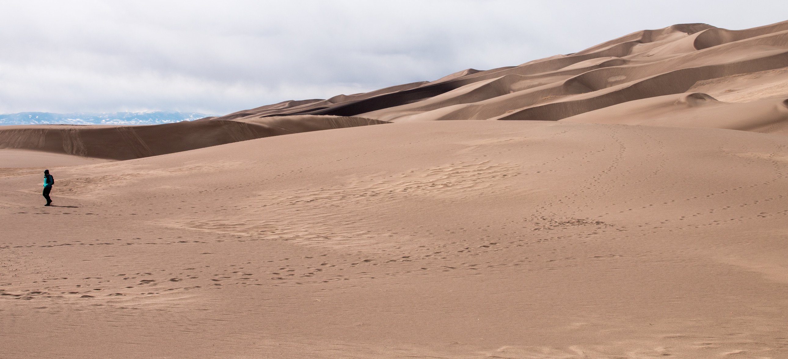 A lone park visitor walks across the dunes as the sun shines. 