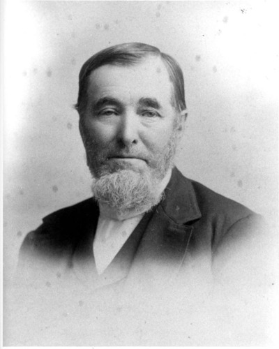 An 1880s photo depicts a man with a white beard showing little emotion.