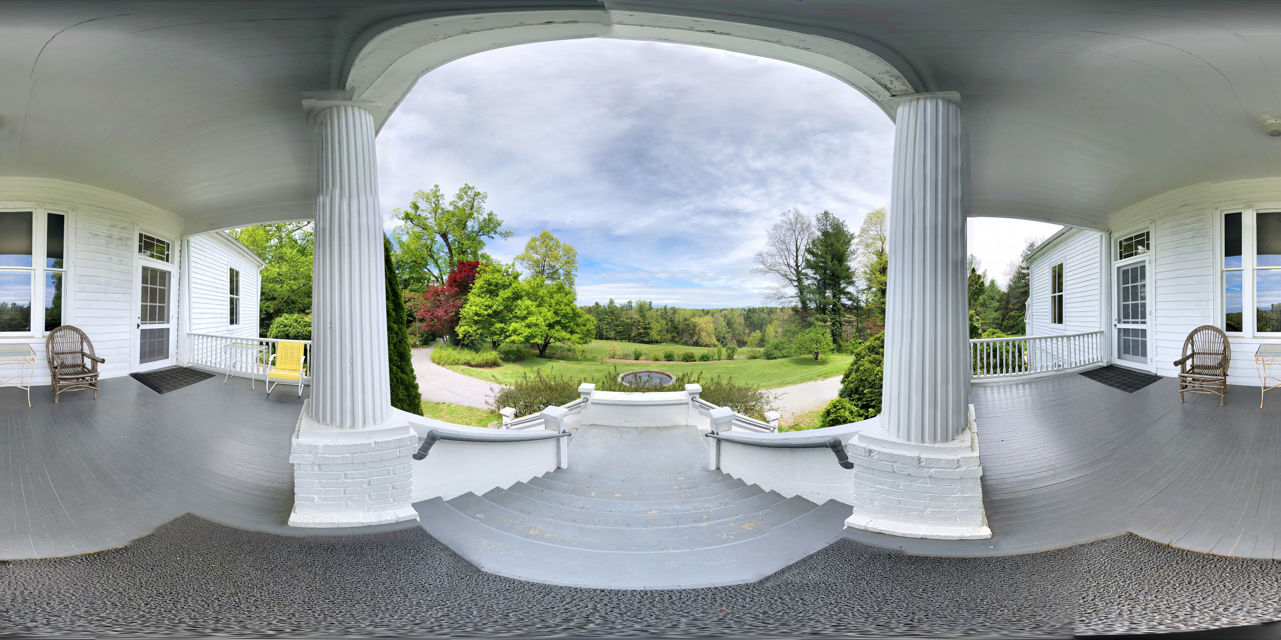 360 degree view from the Sandburg Home porch, including gray wood floors, white columns and views of trees and mountain tops in the distance.