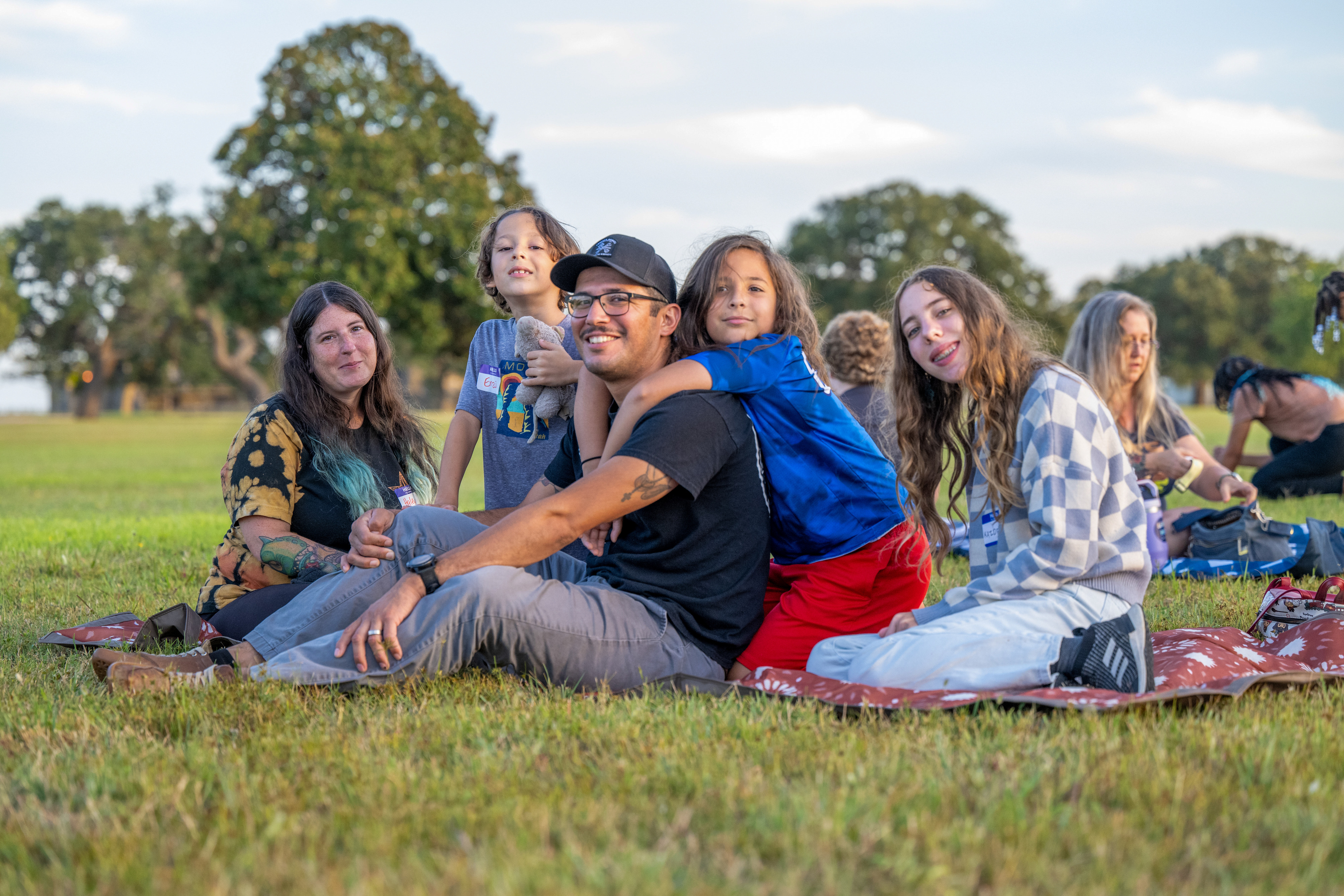 A family of two adults and three children on a picnic blanket pose for a photo.
