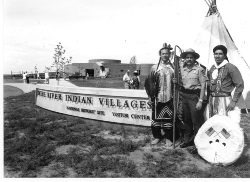 Three men stand in front of the newly constructed Knife River Indian Villages National Historic Site visitor center.