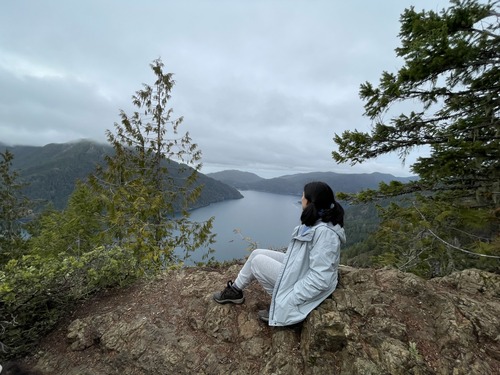 Woman sitting on rocks looking at lake in front of her.