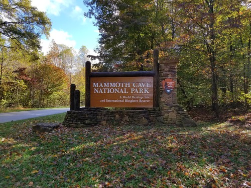 A brown entrance sign with a large stone base and fallen leaves on the ground. 