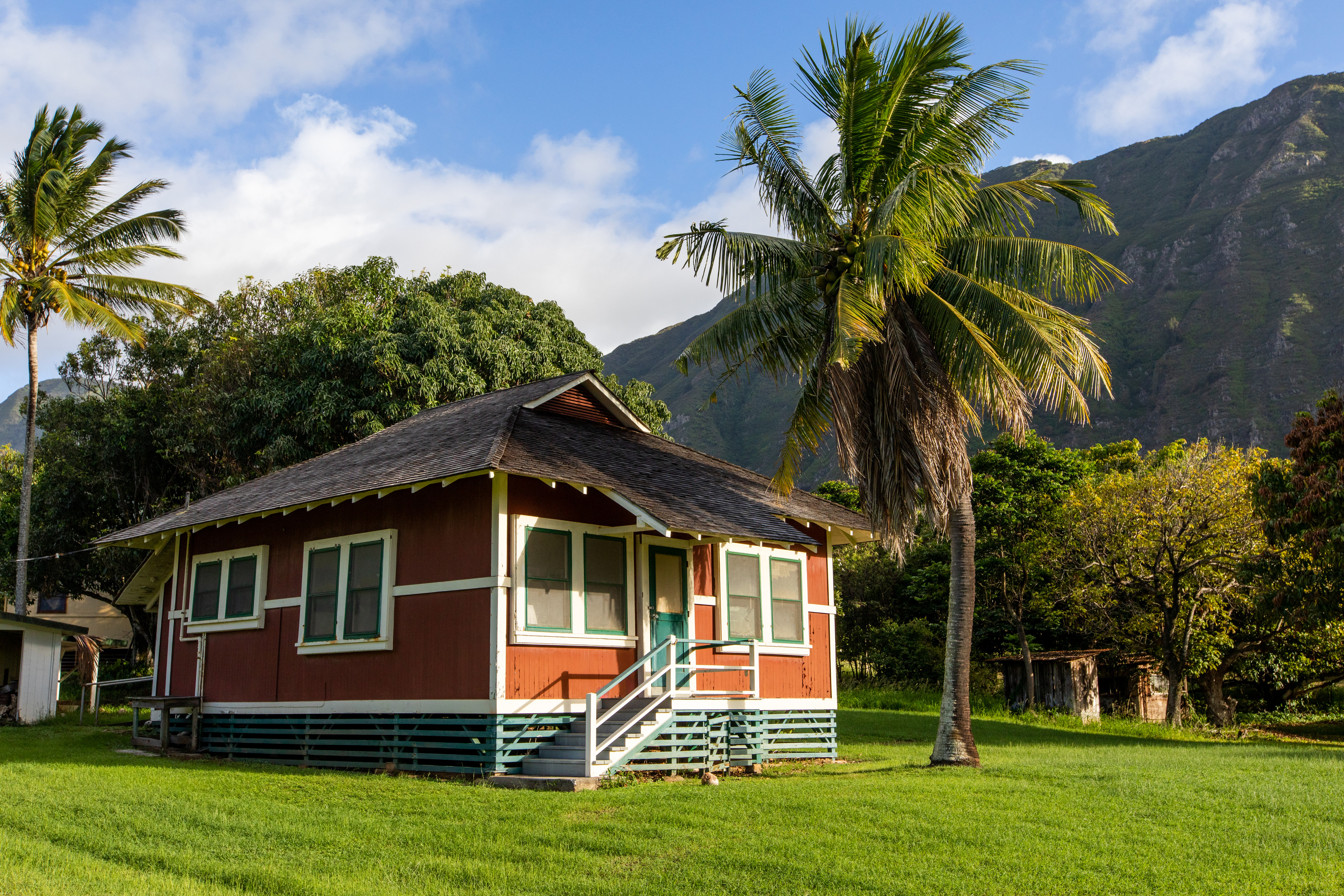 A red building with white and blue windows and doors. A green lawn and trees surround the building. 