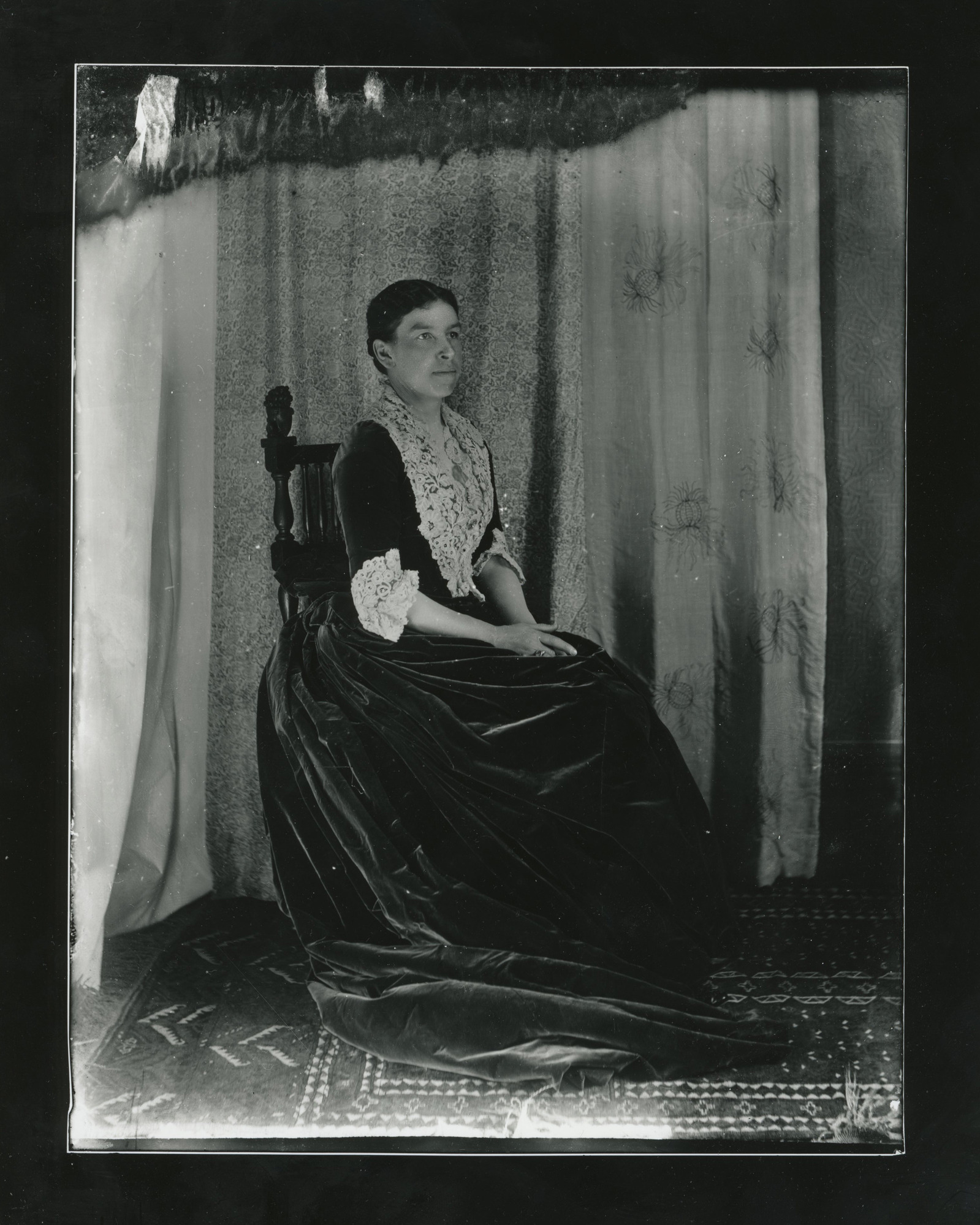 White woman with dark hair seated wearing a velvet dress with lace collar and cuffs.