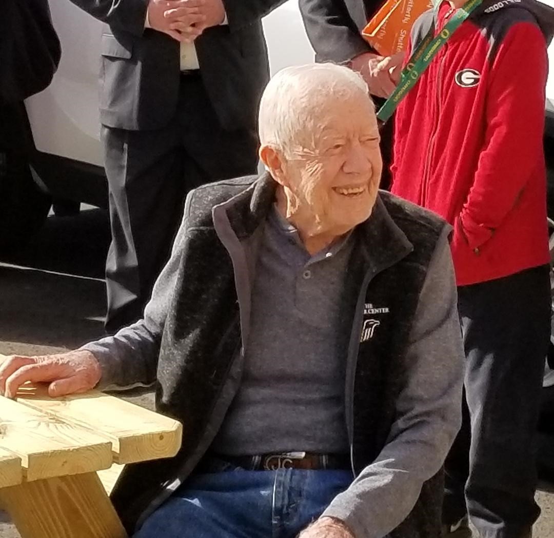 President Carter smiles at guests while seated at a picnic table.