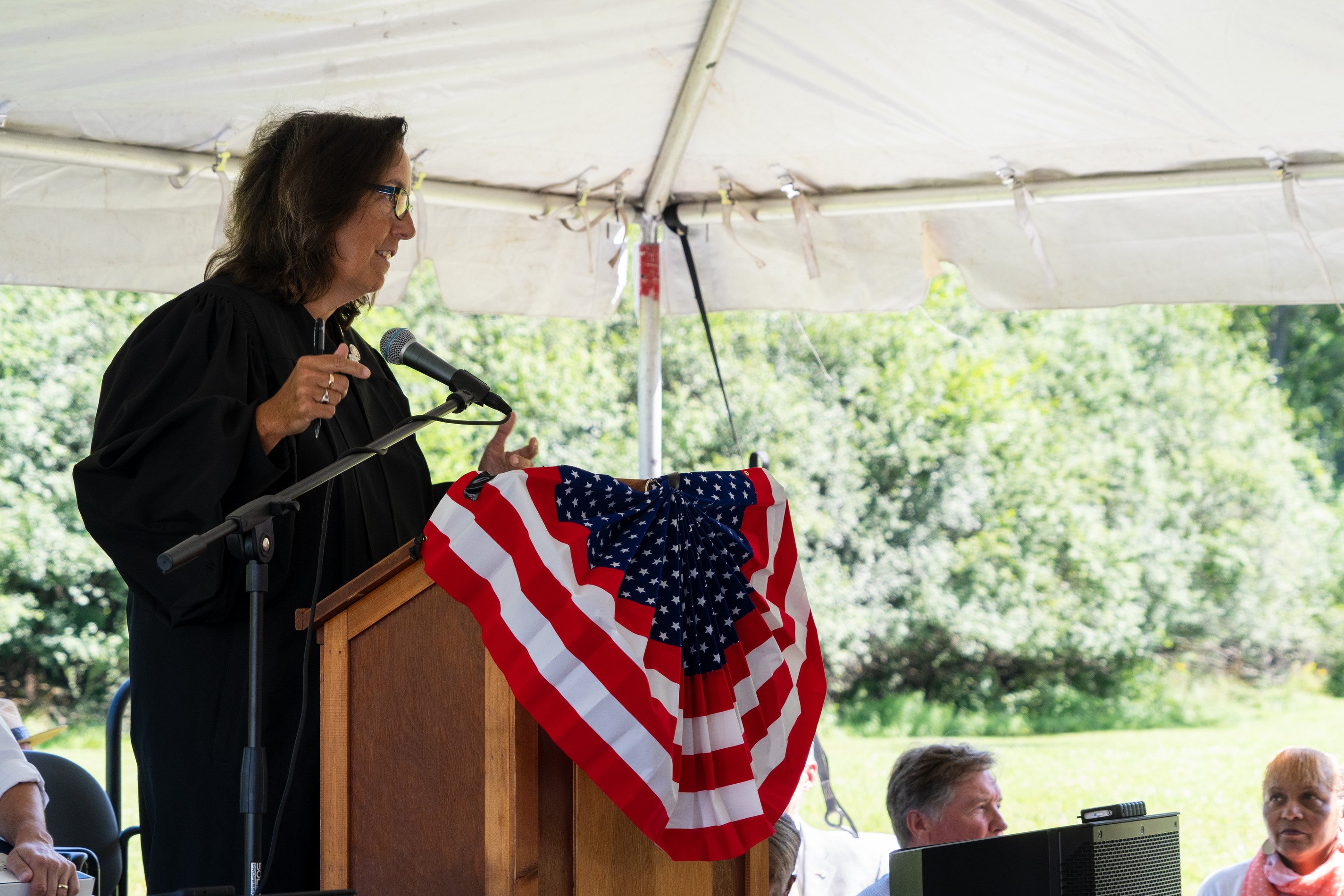 A judge speaks at a podium under a tent.