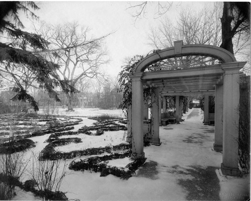 Black and white photograph of garden with arbor in snow.