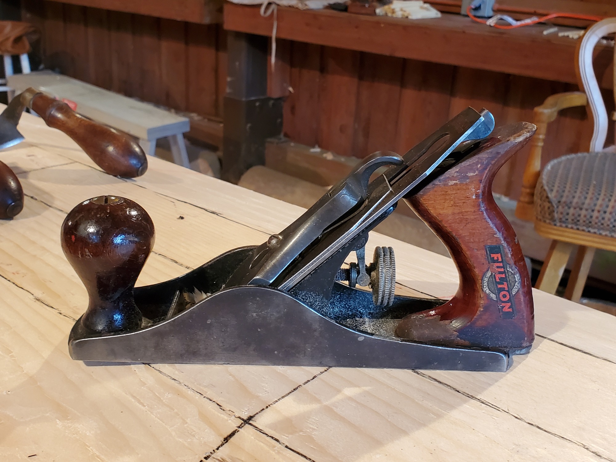 An antique hand plane (carpentry tool) with dark metal body and dark brown handles sits on top of a wood surface.