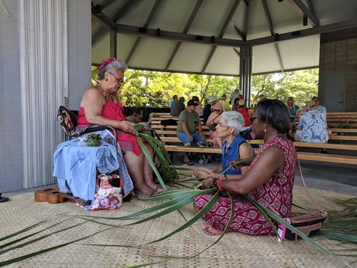 A demonstrator shows two visitors how to weave with coconut leaves in the amphitheater.