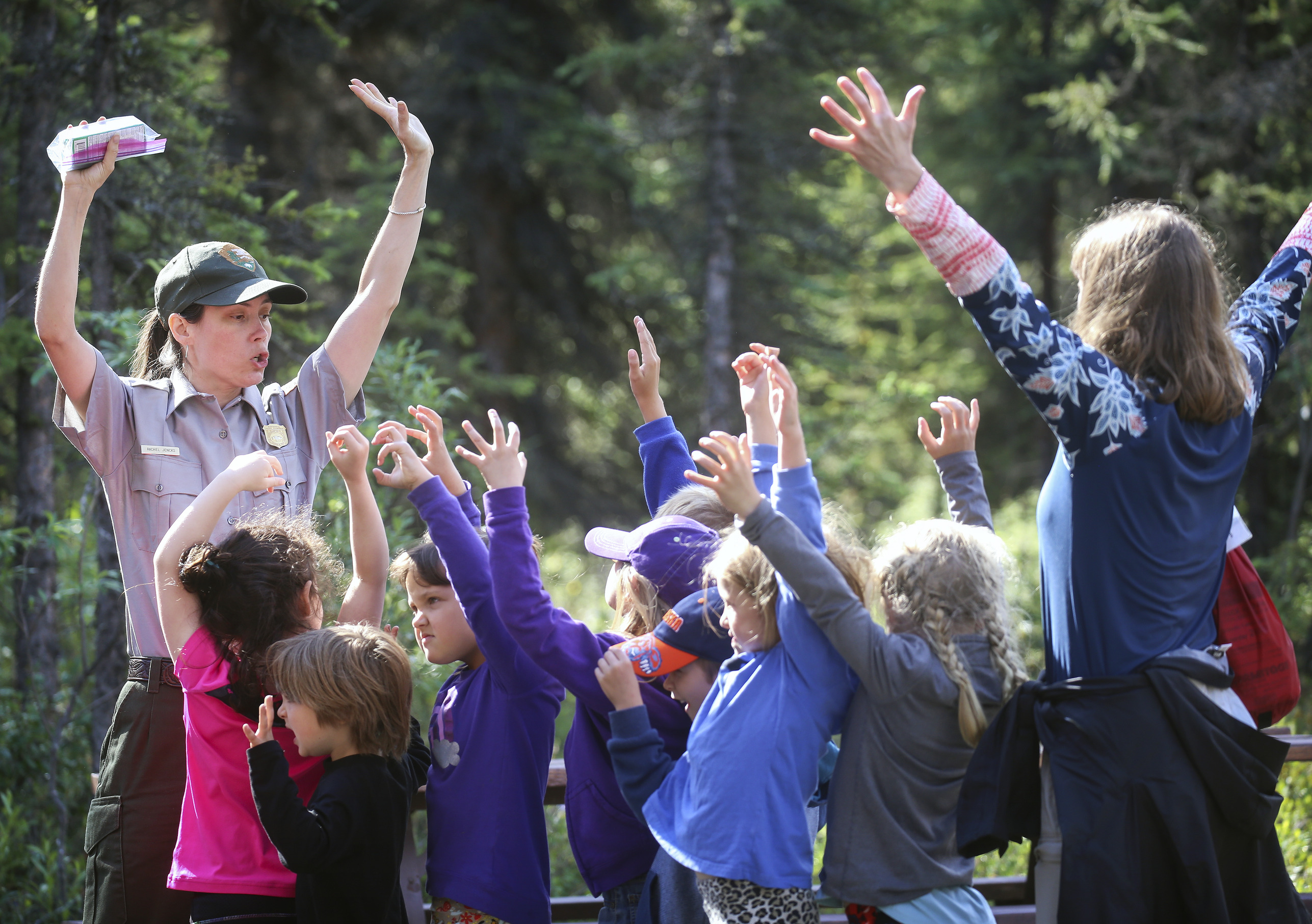 a park ranger and small kids waving their hands over their heads and shouting