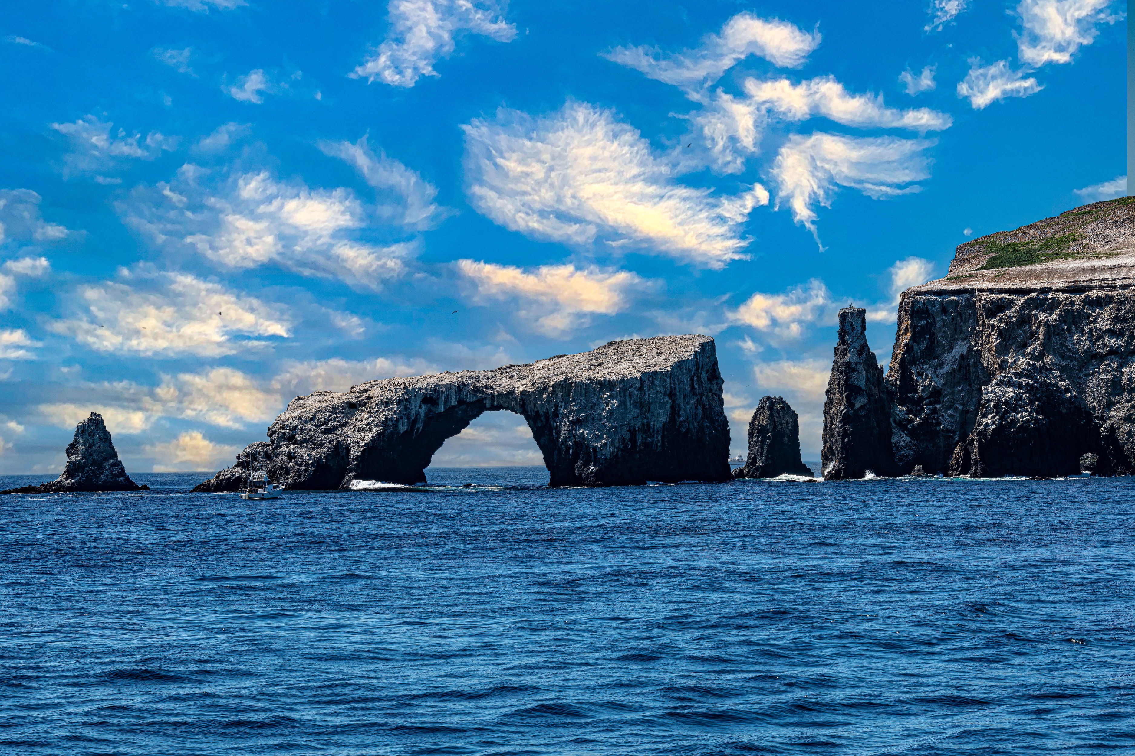 Stone arch extending out into the water. Rippled deep blue water in the foreground and blue sky with wispy light clouds in the background.